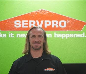 A SERVPRO employee dressed in SERVPRO attire standing in front of a green wall