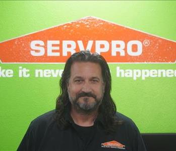 A SERVPRO employee dressed in SERVPRO attire standing in front of a green wall